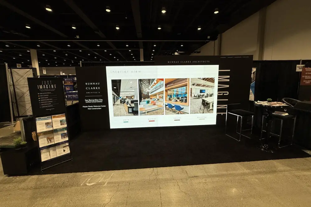 The trade show booth and digital wall I directed, with the Just Imagine rack inviting districts to pick the challenge they're facing and take the matching playbook.
