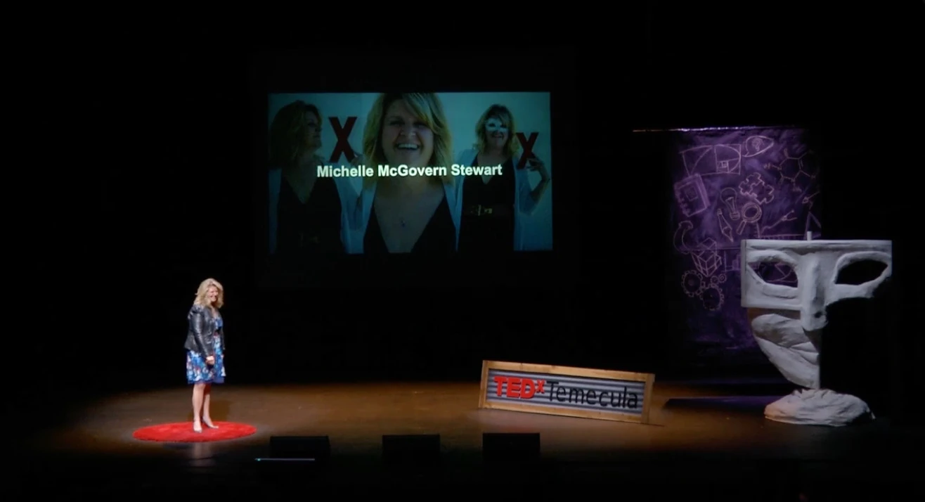 Michelle McGovern Stewart on the red circle at TEDxTemecula, her name on the screen behind her